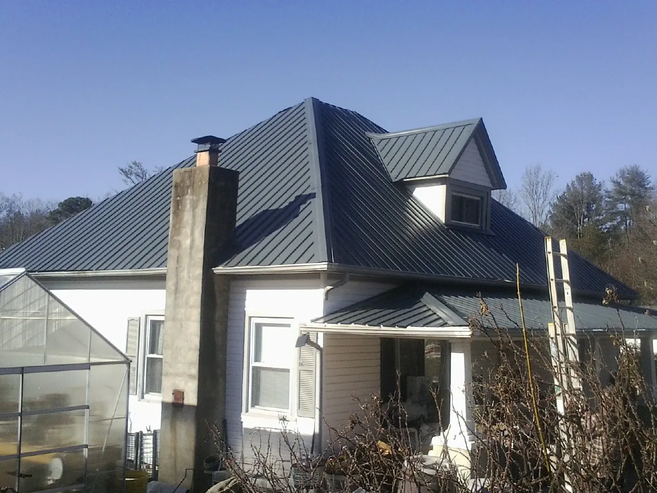 Dark blue standing seam metal roof on a white farmhouse with dormer — Slate & Tile Roof Repair by Roofing Brothers in Chatfield