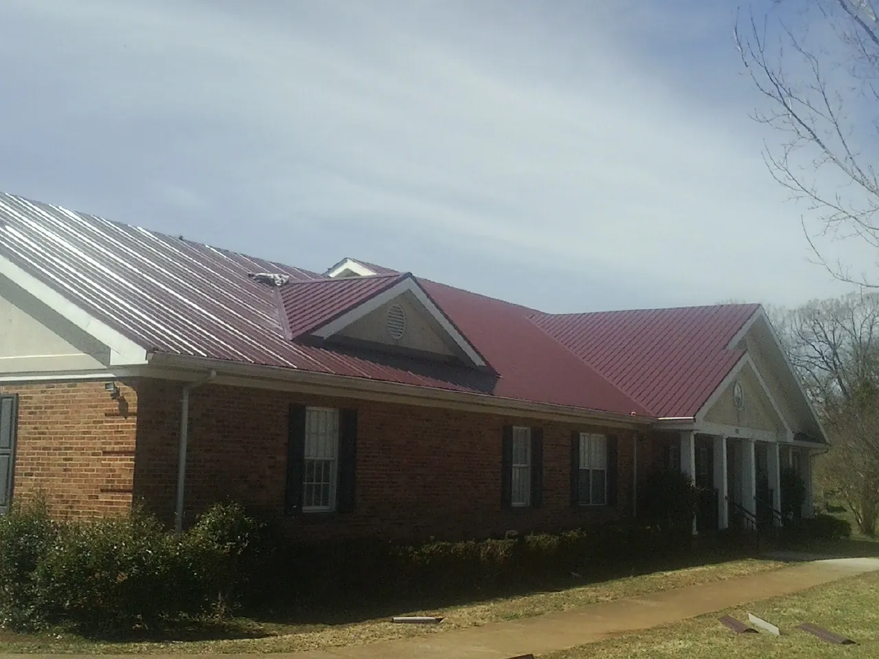 Red metal roof with gabled entries on a long brick building, from a Hail Damage Roof Repair job in Chatfield
