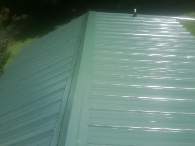 New green metal panels meeting at the ridge of a roof — Flat Roof Repair work by our crew in Chatfield