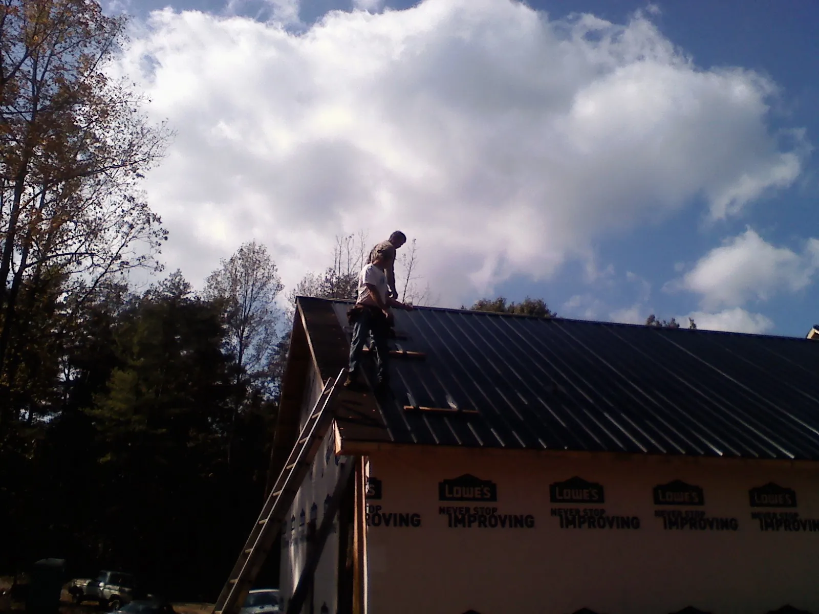 Roofer fastening dark metal panels high against a cloudy sky, from a Roof Inspection job in Chatfield