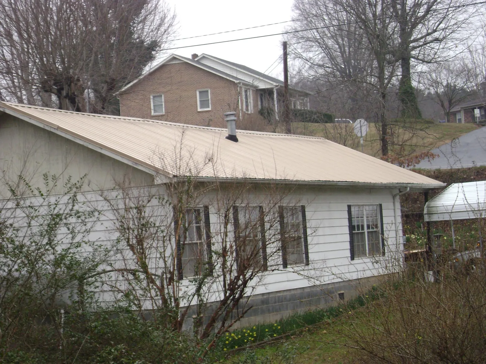 Tan metal roof on a white sided house set into a hillside — Commercial Roofing by Roofing Brothers in Chatfield
