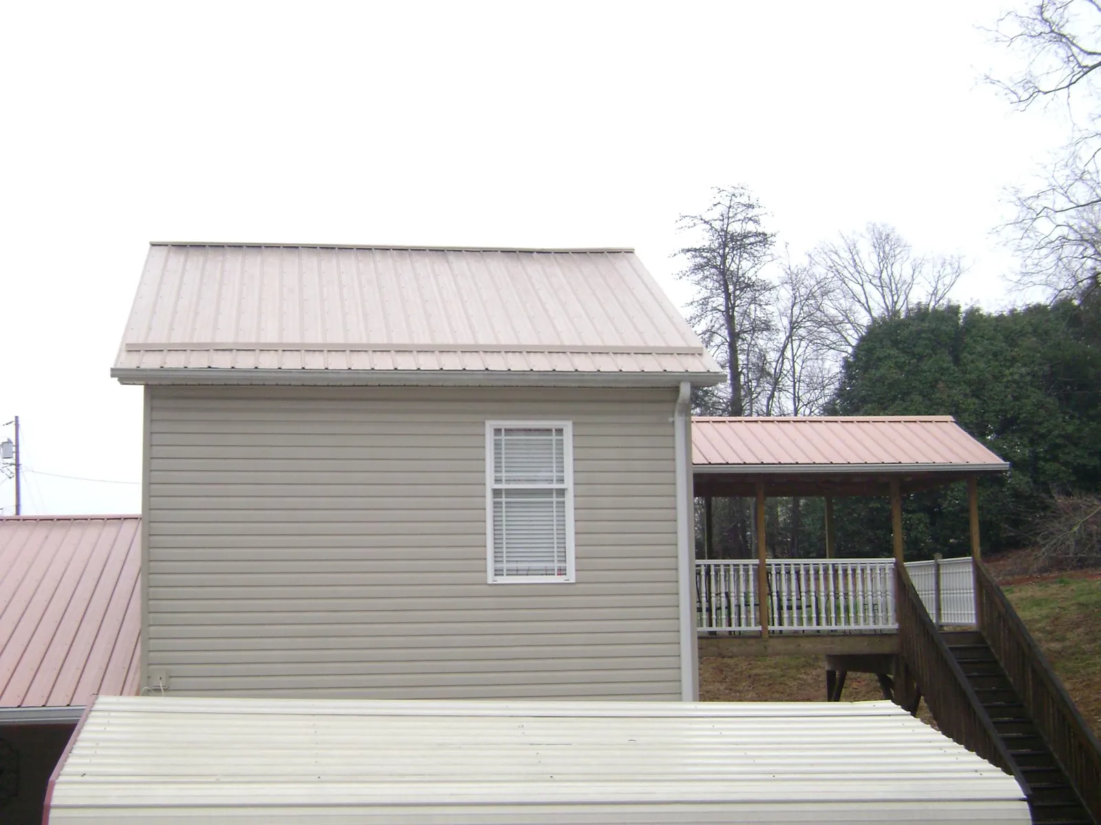 Tan metal roofs on a two story addition and attached porch, from a Roof Replacement job in Chatfield